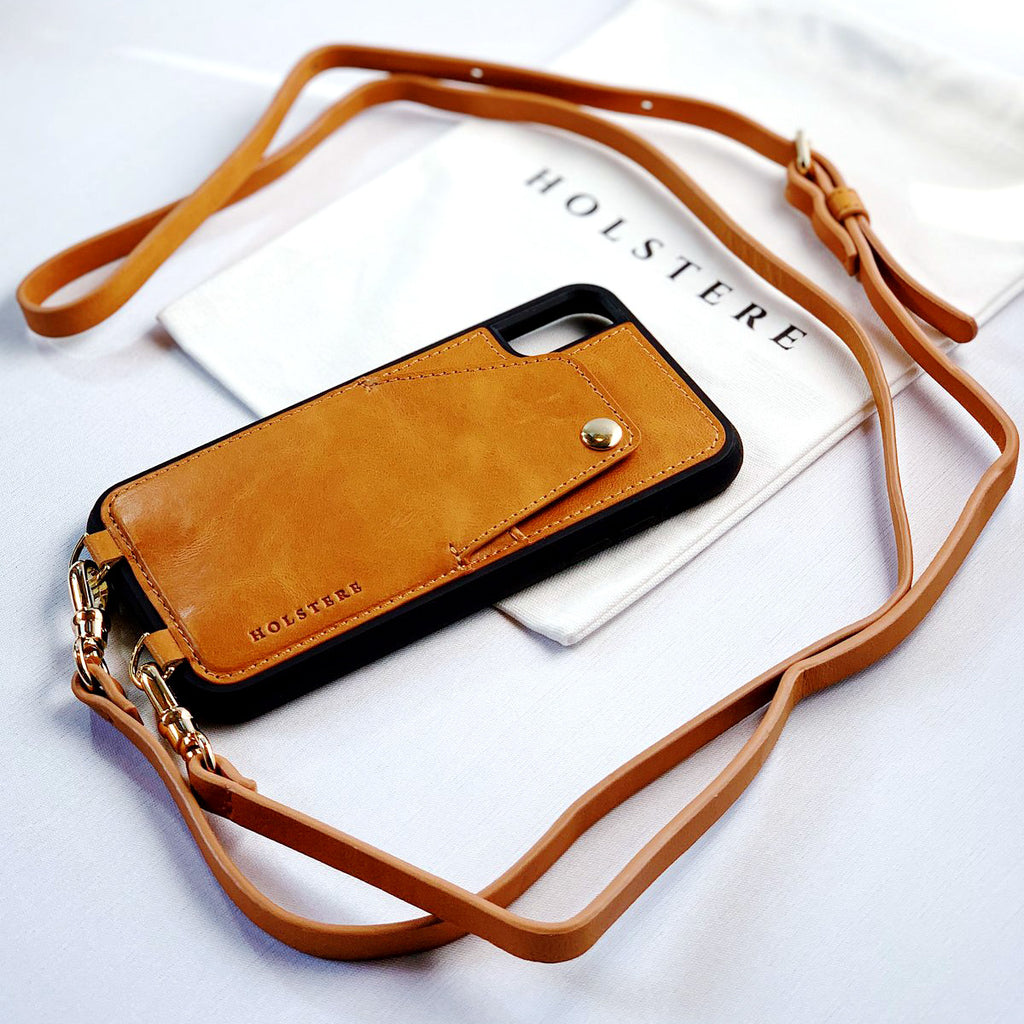 Holster London Tan Leather iPhone case with strap. Free your hands with this luxury iPhone case crossbody in black high-quality smooth leather. Elegant, timeless, and classic with straight lines and detailed stitching for a sleek, polished look. Durable construction offers a modern, sophisticated, chic look. Leather finish feels luxurious to the touch. Case fully wraps around iPhone for ultimate protection.